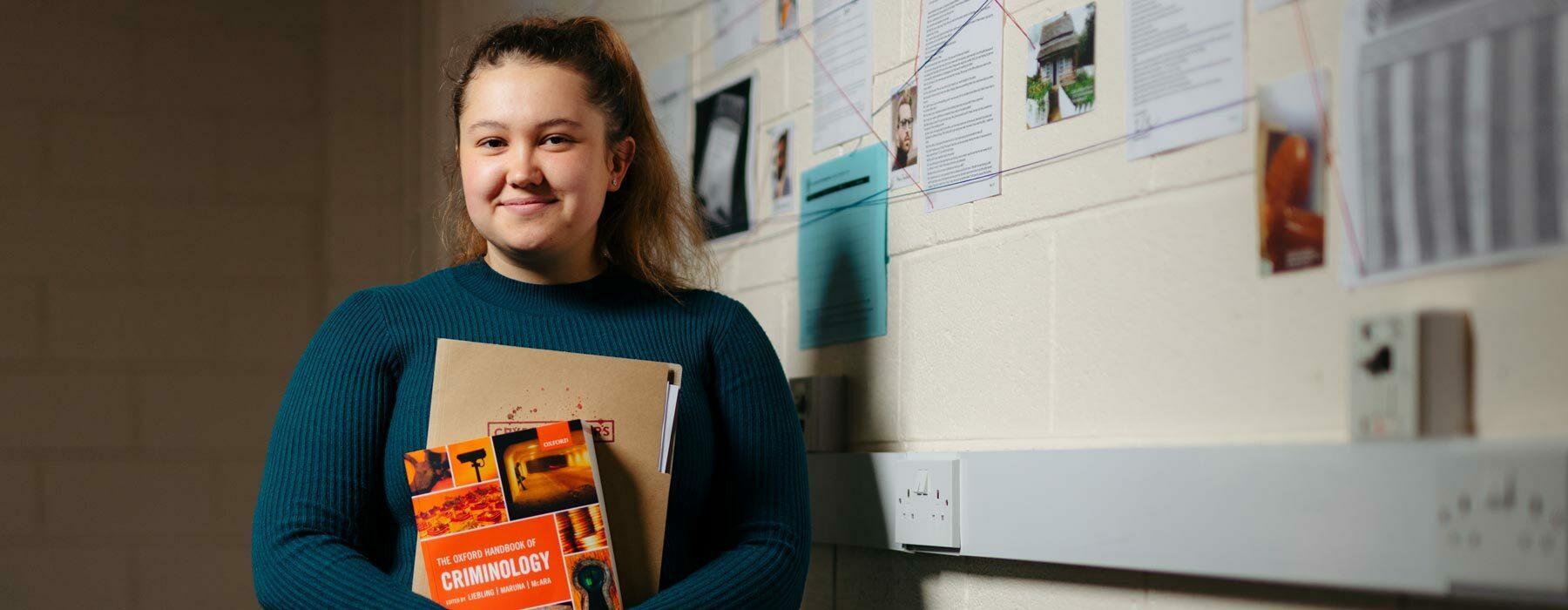 Crimin banner Degree student holding Criminology books in front of evidence wall