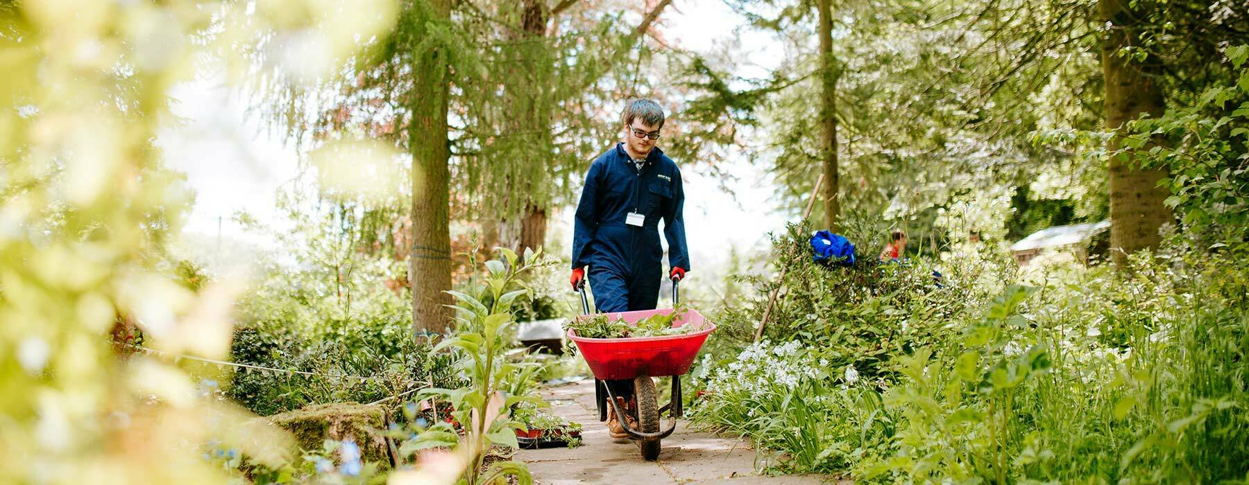 Horti banner Horticulture student walking through gardens with wheelbarrow